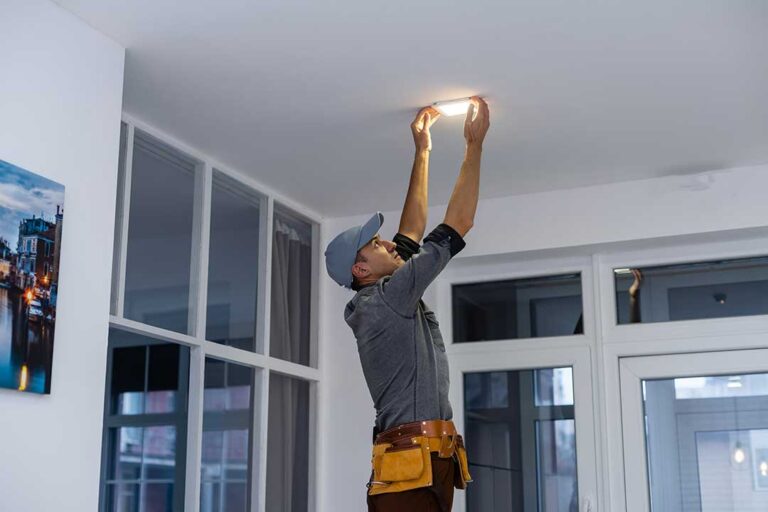 A close-up of a person inspecting a standard wall outlet with visible scorch marks.