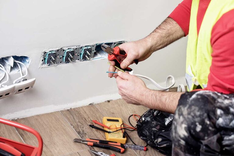 A homeowner carefully replacing a wall outlet using insulated tools in a well-lit living room.